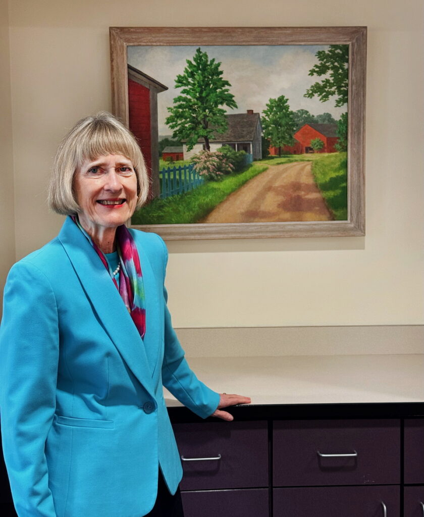 Columbia-Greene's Dr. Carlee Drummer, with an oil painting of the Benham family farm, which hangs in the president's office. Photo by Annik LaFarge, author of Composing Olana