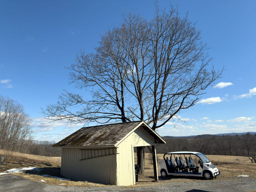 The privy at Cosy Cottage, with an electric vehicle attached to a charging cable, February 2025. Photo by Annik LaFarge, author of Composing Olana